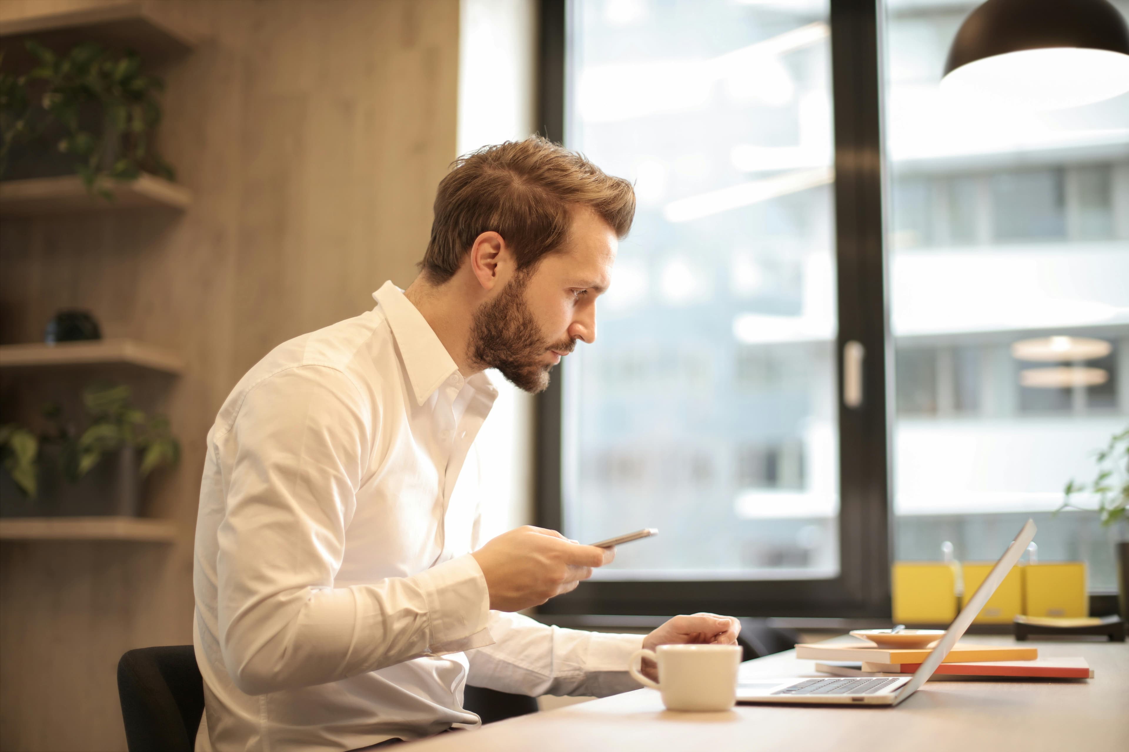 Man holding his phone and looking at his computer